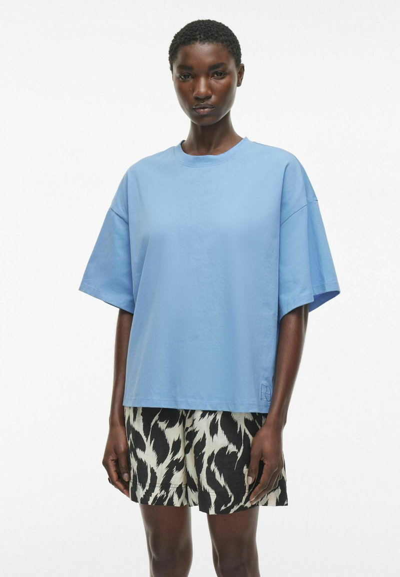 Lys blå oversized t-skjorte i bomull, med rund hals og korte ermer, sammen med svarte og hvite mønstrede shorts.