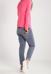 Camicia rosa a maniche lunghe con fessure laterali, abbinata a jeans blu chiaro a vestibilità comoda con orli arrotolati e tasche, indossata con sneakers grigie.