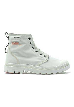 Bottes montantes blanches en tissu respirant avec une semelle en caoutchouc, dotées d'œillets noirs, d'une languette et d'accents de texte rouges.