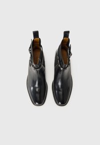 Bottines en cuir noir avec une finition lisse, bout pointu et accents décoratifs en métal argenté sur le côté. Talon plat et tirant.