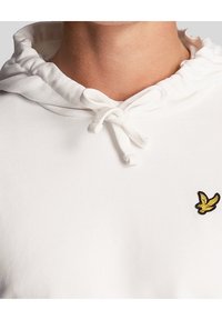 Felpa bianca realizzata in tessuto morbido, con cappuccio regolabile e un piccolo logo di un uccellino ricamato di colore giallo sul petto.