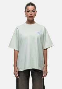 T-shirt oversized verde chiaro realizzata in morbido cotone, con scollatura rotonda e maniche corte, decorata con dettagli stampati blu sul petto.