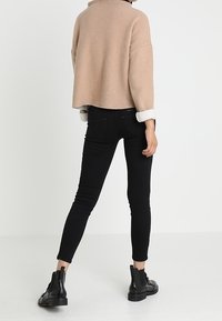 Avkortad beigesweater med hög krage, i kombination med svarta skinny jeans och svarta ankelstövlar, med en slät textur och tight passform.