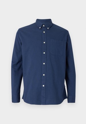 Camisa azul marino de manga larga con cuello tipo button-down, botones blancos y un bolsillo en el pecho izquierdo sobre un fondo blanco.