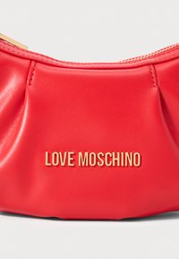 Röd läderdesignerpouch med guldfärgad dragkedja och centrerad guld "LOVE MOSCHINO" logotyptext framtill.