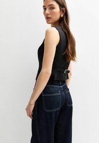 Haut sans manches noir avec un design structuré, présentant un détail de boucle à l'arrière. Assorti à un jean bleu foncé taille haute. Texture de tissu lisse.
