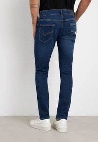 Jeans slim fit blu scuro con lavaggio medio, dotati di due tasche posteriori con cuciture a contrasto e dettagli in vita nera.