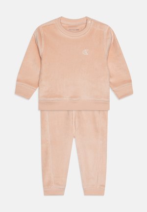 Conjunto de chándal de pana en color melocotón que incluye una parte superior de manga larga con bordes cosidos y pantalones a juego con puños elásticos. Cuello ajustable.