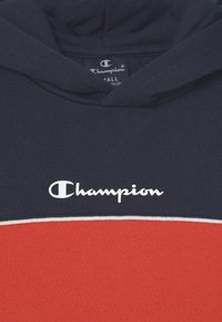 Sudadera con capucha en color marino y rojo, fabricada en algodón. Presenta un logotipo blanco en el pecho y una franja blanca en contraste entre los colores.