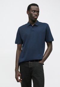 Polo-shirt à manches courtes bleu marine avec col, fabriqué à partir d'un tissu texturé, avec un logo subtil sur la poitrine et une coupe décontractée.