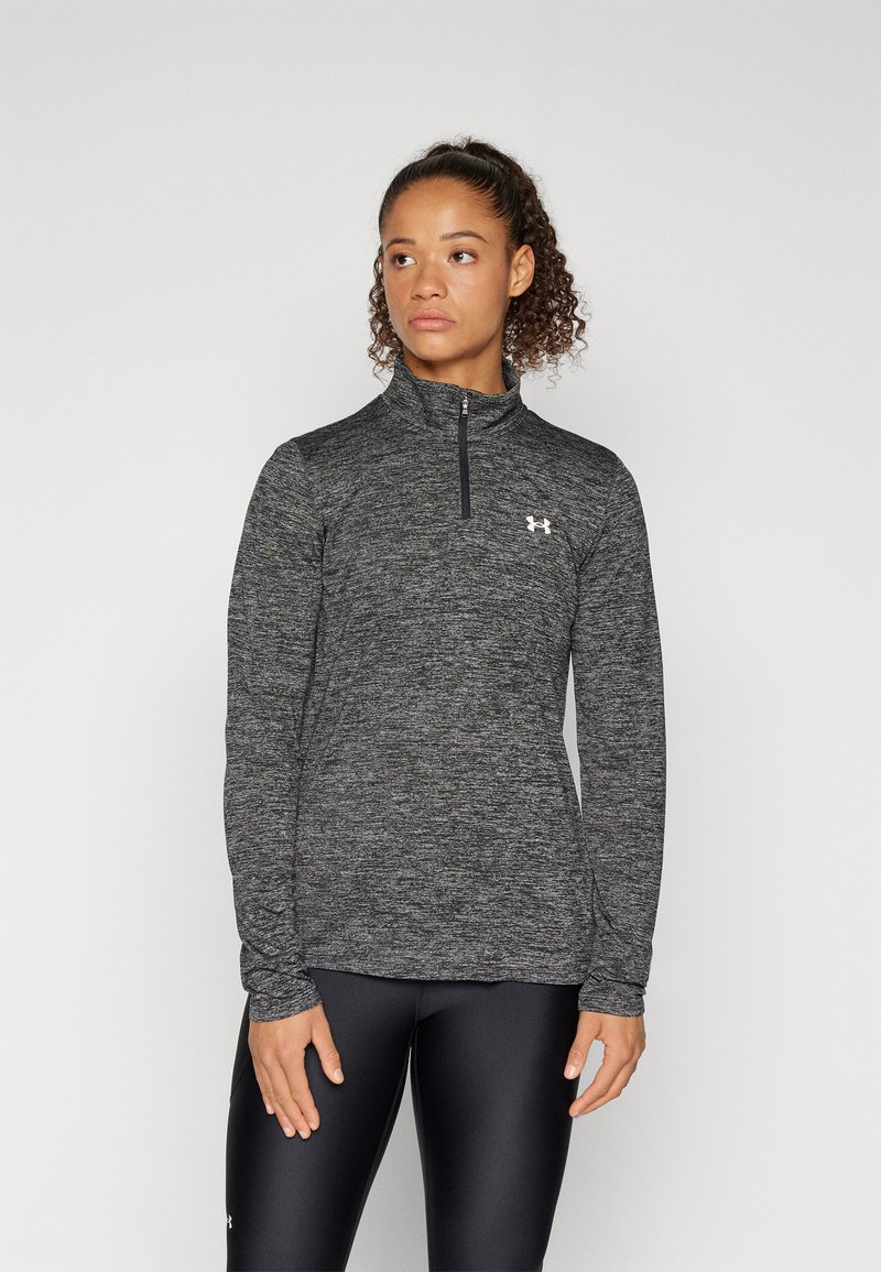 Schwarzes Heideremmershirt mit Viertel-Reißverschluss und langen Ärmeln, glatter Textur, sportlichem Schnitt und Logo auf der Brust, kombiniert mit schwarzen Leggings.