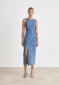 Denim midi haljina u svijetloplavoj boji s prednjim prorezom, bočnim kopčama i okruglim izrezom. Uparena s srebrnim sandalama na visoku petu. Glatka tekstura.