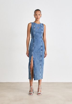 Denim midi haljina u svijetloplavoj boji s prednjim prorezom, bočnim kopčama i okruglim izrezom. Uparena s srebrnim sandalama na visoku petu. Glatka tekstura.