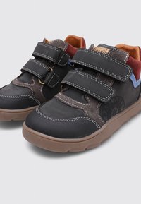 Zapatos negros y marrones con correas de velcro, que presentan una mezcla de materiales lisos y texturizados, suelas de goma y acentos coloridos.