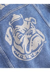 Veste en denim avec une texture bleue et un imprimé graphique de bulldog blanc, situé sur la zone de la poitrine gauche, avec des détails de couture jaunes.