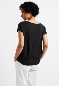 T-shirt noir à manches courtes avec un col rond, coupe décontractée et un ourlet arrière légèrement plus long, associé à un pantalon blanc.