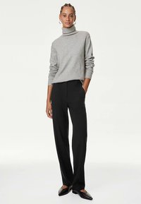 Grå polotröja med långärmar, kombinerad med svarta skräddarsydda byxor och svarta loafers, visad mot en neutral bakgrund.