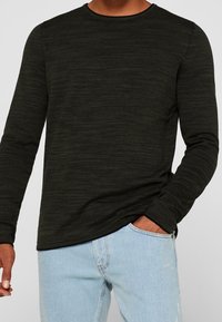 Czarny longsleeve wykonany z fakturowanej tkaniny z delikatnym wzorem w paski. Okrągły dekolt i dopasowany krój, w połączeniu z jasnoniebieskimi dżinsami.