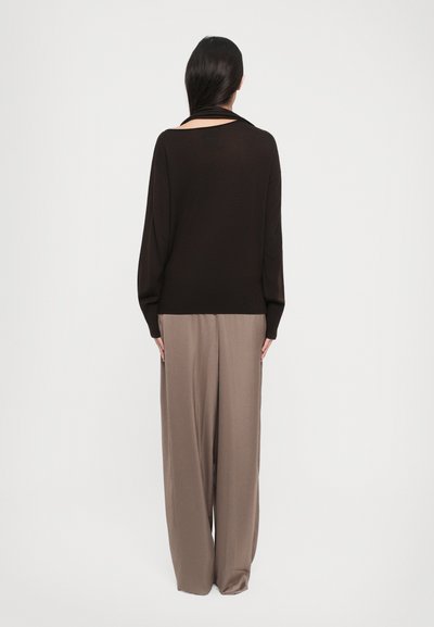 Black knitted sweater with a loose fit, wide sleeves, and a scoop back, paired with loose beige trousers made of soft fabric.