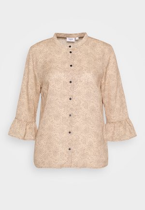 Beigenvärinen pitkähihainen pusero, jossa musta pilkullinen kuvio, mustat napit edessä, röyhelöhihansuut ja pyöreä pääntie.