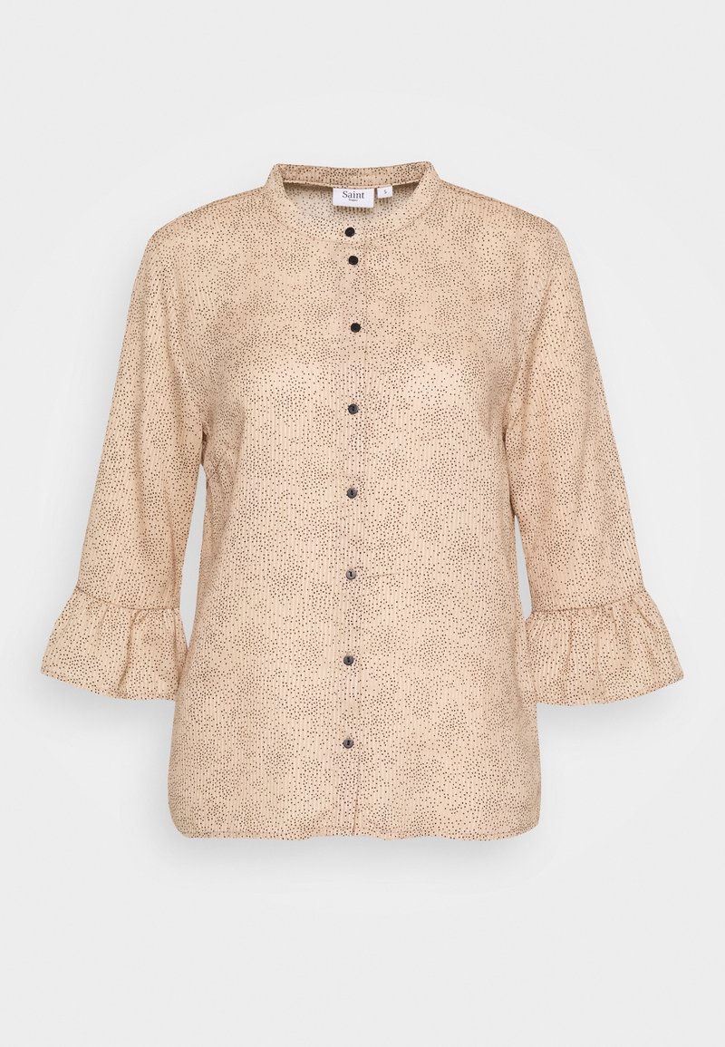 Blouse beige à manches longues avec un motif noir tacheté, boutons noirs sur le devant, poignets à volants et col rond.
