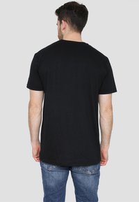 Black cotton t-shirt with short sleeves, crew neck, and a smooth texture. Visible seams and casual fit. Worn with blue jeans.