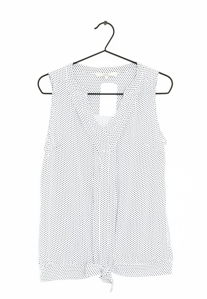 Blouse sans manches blanche à pois noirs, décolleté en V et détail de ourlet noué. Tissu léger, suspendue à un cintre noir.