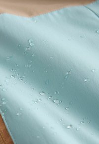 Lichtblauwe waterdichte stof met meerdere waterdruppels die op het oppervlak parelen, wat waterbestendigheid aangeeft.