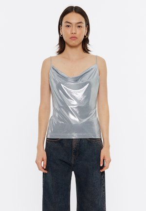 Top sin mangas de cuello en cowl de color plateado con tirantes delgados. Material brillante, diseño ajustado y textura suave. Combinado con jeans de pierna ancha oscuros.