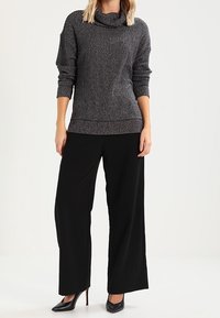 Šedý pletený svetr s rolákem, kombinovaný s černými kalhotami s širokými nohavicemi. Kompletní vzhled doplňují černé lodičky na vysokém podpatku.