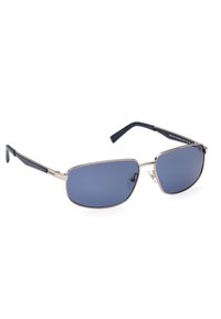 Occhiali da sole con montatura in metallo argentato, lenti blu scure e terminali in plastica nera. Caratteristiche includono le imbottiture per il naso e un design rettangolare elegante.