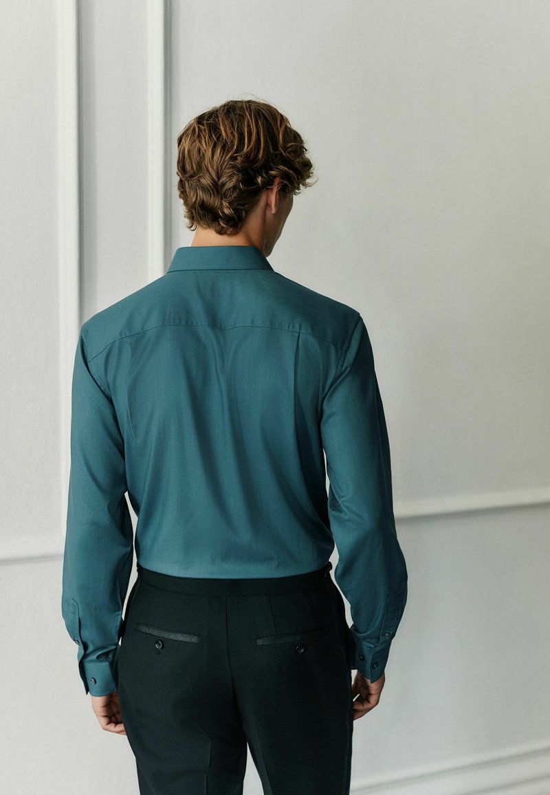 Teal long-sleeve shirt with a collar and buttoned cuffs, paired with black pants featuring back pockets and a smooth texture.