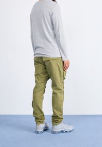 Grijs longsleeve shirt gecombineerd met olijfkleurige cargobroek en grijze sneakers. De broek heeft zakken en een relaxte pasvorm. Glad stoftextuur.