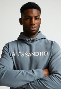 Sudadera gris con el texto bordado en blanco "ALESSANDRO". La tela es suave y cuenta con capucha con cordón y puños acanalados.