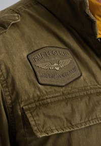 Veste olive avec un patch brodé portant la mention "PME Legend American Classic". Dispose d'un tissu texturé et d'une poche poitrine.
