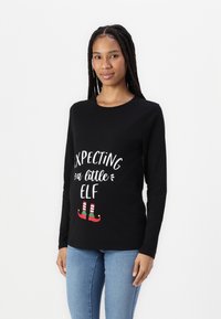 Black long-sleeve shirt featuring white text “Expecting a little ELF” and red-green striped elf shoes graphic. Soft fabric, standard fit.