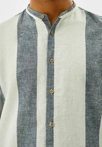 Overhemd met knoopsluiting, voorzien van horizontale strepen in lichtbeige en donkerblauw-grijs linnen, met een bandkraag en houten knopen.