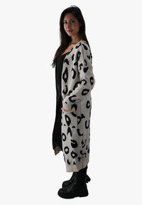 Cardigan lungo aperto di colore crema con un design in stampa leopardata nera. Tessitura a maglia con polsini a costine e tasche laterali.