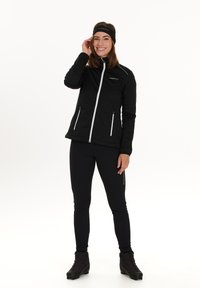 Musta urheilu takki, jossa on valkoinen vetoketju ja korostukset, yhdistetty mustiin legginsseihin ja saappaisiin. Mallilla on päässään yhteensopiva musta hiuspanta. Tasainen pinta.