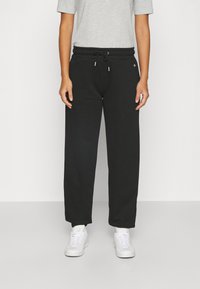 Schwarze Baumwoll-Sweatpants mit elastischem Bund, verstellbarem Kordelzug und vorderen Taschen. Kombiniert mit einem grauen T-Shirt und weißen Sneakers.