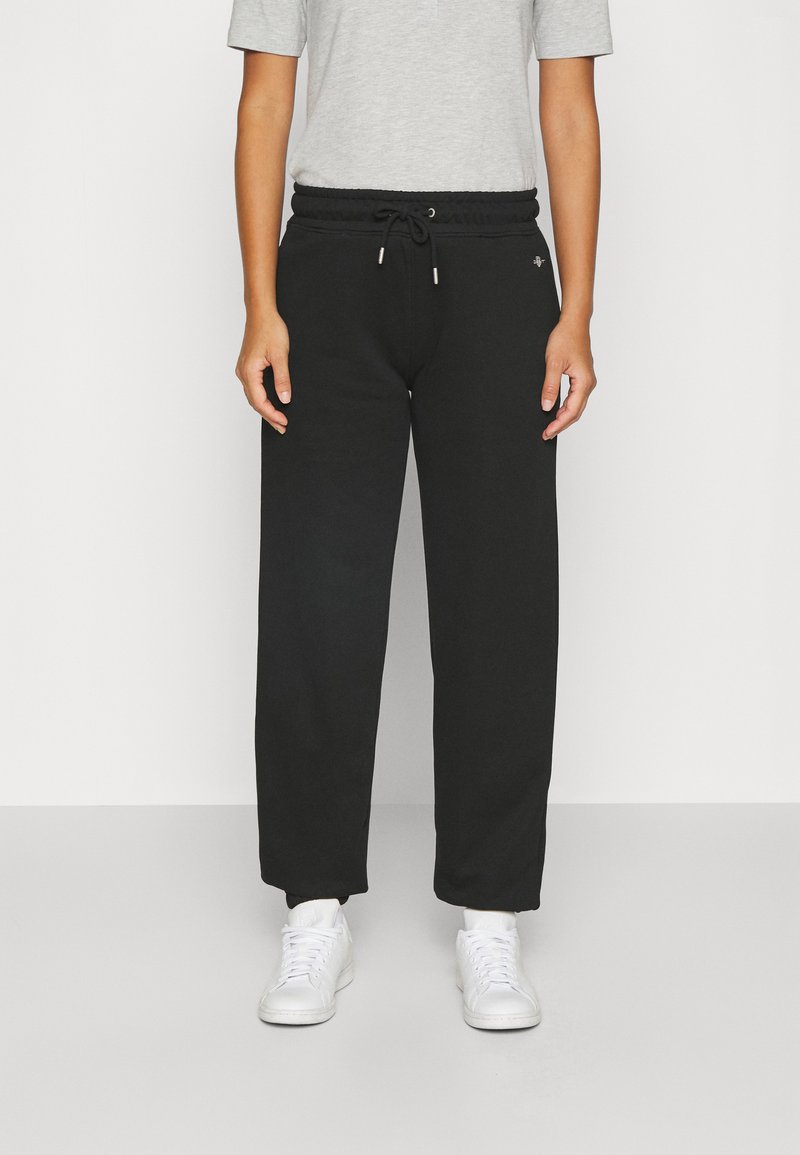 Schwarze Baumwoll-Sweatpants mit elastischem Bund, verstellbarem Kordelzug und vorderen Taschen. Kombiniert mit einem grauen T-Shirt und weißen Sneakers.