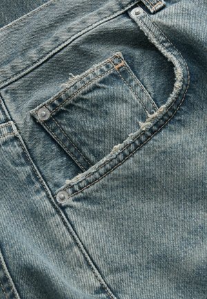 Hellblaue Denim mit abgenutzter Textur, ausgestattet mit einer kleinen Gesäßtasche, die durch silbernes Beschlagsmaterial gesichert ist, und ausgefransten Rändern entlang der Taschenöffnung.