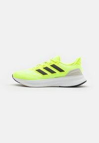 Zapatillas deportivas amarillas con parte superior de malla, rayas negras y suela blanca. Presentan un talón acolchado y detalles texturizados en la parte superior.