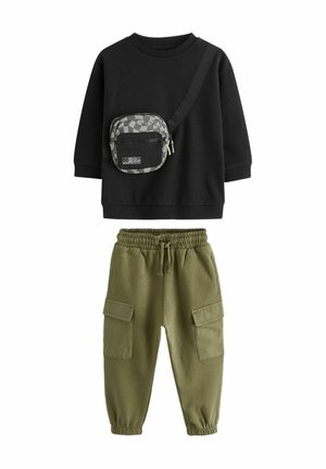 Sudadera negra con un bolso cruzado de patrón a cuadros. Pantalones jogger verde oliva con puños elásticos y grandes bolsillos laterales.