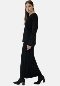 Zwart geribd gebreid tweedelig set bestaande uit een top met lange mouwen en een vloerlang rokje, gecombineerd met zwarte enkellaarsjes met hak.