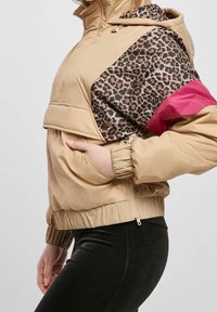 Kurtka puchowa w kolorze brązowym z panterkowym nadrukiem na rękawach i różowymi akcentami. Posiada kieszeń na zamek, elastyczne mankiety i luźny krój.