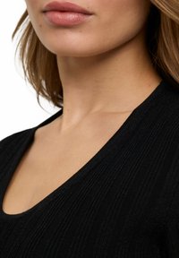 Czarny top o teksturowej powierzchni z dekoltem w kształcie litery V, z pionowym prążkowanym detalem, gładkim materiałem oraz dopasowanym krojem.