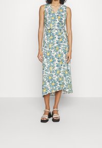 Kukalla midi mekko, jossa on V-nick, olkaimeton malli, sinisiä ja keltaisia kuvioita kerma-taustalla, vyötetty vyötärölle.