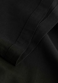 Tissu noir à texture lisse, avec des bords pliés et des coutures visibles. Le tissu est léger et d'apparence mate.