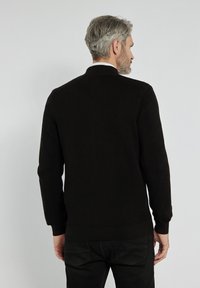 Czarny sweter dzianinowy z długimi rękawami i okrągłym dekoltem. Tekstura jest prążkowana, pokazująca jednolity wzór z dopasowanym dołem.